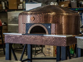 Fiero pizza oven covered in gold tiles and with black legs